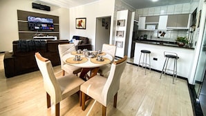 Una sala de estar moderna con comedor, una cocina con armarios blancos y un televisor montado en la pared.