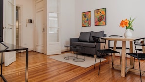 A modern living room with a wooden floor, a grey sofa, a dining table with chairs, and two framed artworks on the wall. - Alvear Bioy Residence by Argenhost (Buenos Aires)