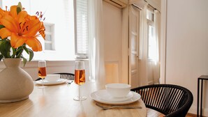 A dining table with a vase of orange flowers, two glasses of amber liquid, and white dishes. - Alvear Bioy Residence by Argenhost (Buenos Aires)
