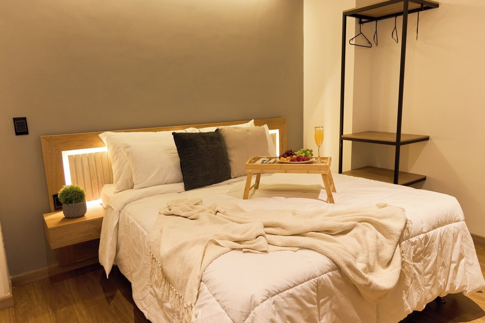 A neatly made bed with a bedside table, a small plant, and a tray with fruit and a glass of orange juice.