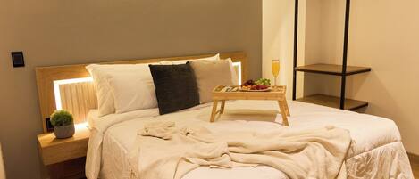 A neatly made bed with a bedside table, a small plant, and a tray with fruit and a glass of orange juice.