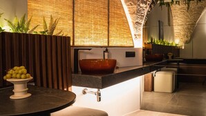 Un baño moderno con un ventanal grande, un panel de pared de madera, un lavabo redondo y un frutero sobre un pedestal.
