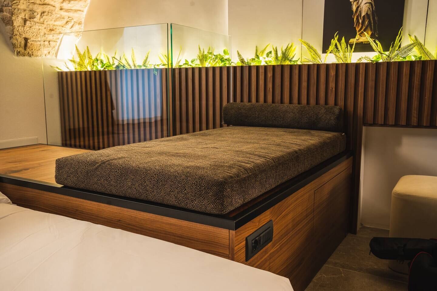 A modern bedroom with a wooden platform bed, a glass-top bedside table, and a wall-mounted plant display.