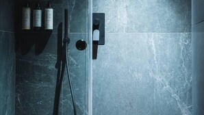 Una ducha moderna con puerta de vidrio, cabezal de ducha de mano y un aplique vertical.