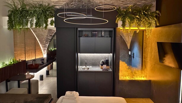Una habitación de hotel moderna con techo de piedra, cocina integrada y cama con toalla doblada con cuidado.