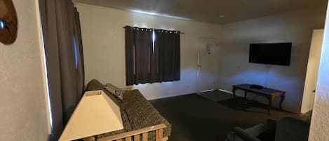 Una sala de estar compacta con un sofá, una mesita, un televisor y una puerta con cortinas.