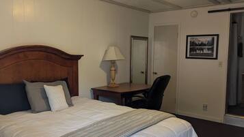 A hotel room with a large bed, a desk with a lamp, a chair, a mirror, and a framed picture on the wall.