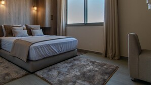 Un dormitorio moderno con una cama grande, cabecera de madera, un sofá y vistas al cielo a través de una ventana.