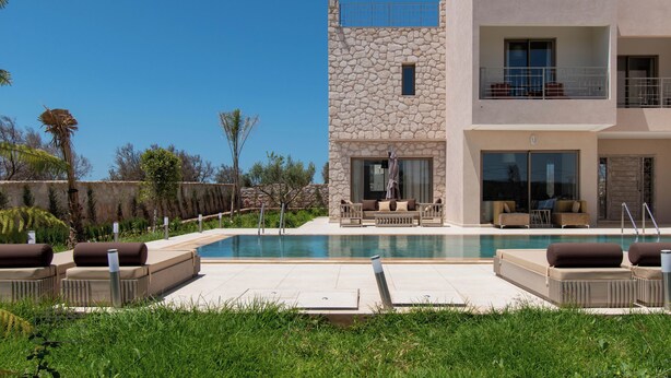 Un edificio moderno de dos pisos con fachada de piedra, piscina y asientos exteriores.