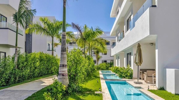 A modern hotel with a swimming pool, palm trees, and a well-maintained garden. - Family-Friendly White Sands 2BR - Private Pool, Fast Wi-Fi, Near Beach (Punta Cana)