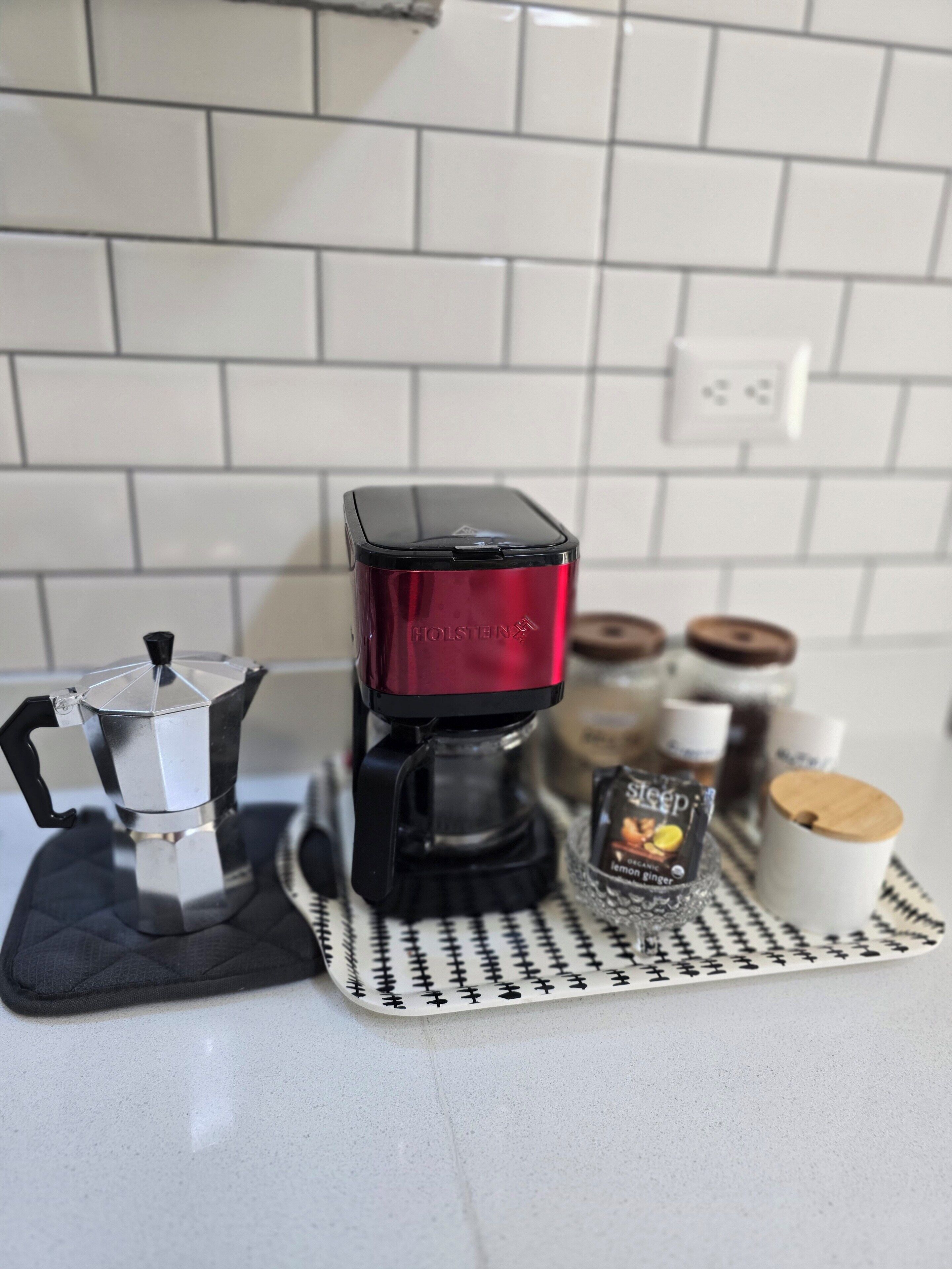 Een keuken met een koffiezetapparaat, een mokka-kan en diverse keukengerei op een aanrecht.