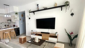A modern living room with a sofa, coffee table, and TV. There is a kitchen area with a sink and cabinets. - Family-Friendly White Sands 2BR - Private Pool, Fast Wi-Fi, Near Beach (Punta Cana)
