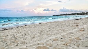 A beach with a clear sky and calm sea, featuring footprints and a distant shoreline with trees. - Family-Friendly White Sands 2BR - Private Pool, Fast Wi-Fi, Near Beach (Punta Cana)
