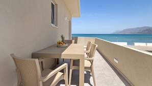Un balcon avec une table et des chaises, un panier de fruits et une vue sur la mer et les montagnes.