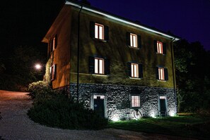Un bâtiment à deux étages, avec une base en pierre et une partie supérieure jaune, doté de nombreuses fenêtres et d’un petit espace extérieur aménagé pour s’asseoir.
