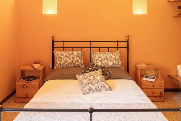 Cama com estrutura metálica, duas mesas de cabeceira de madeira e almofada estampada.