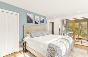A bedroom with a bed, a nightstand, a window with a view of trees, and a door. - Mountain Views, Hot Tub, Impeccable Design (Wintergreen Resort)