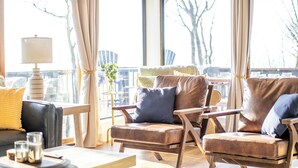 A modern living room with leather sofas, a wooden coffee table, and a floor lamp. Large windows offer a view of the outdoors. - Mountain Views, Hot Tub, Impeccable Design (Wintergreen Resort)