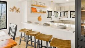 A modern kitchen with white cabinetry, wooden bar stools, and decorative wall art. - Mountain Views, Hot Tub, Impeccable Design (Wintergreen Resort)