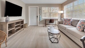 A living room with a sofa, a coffee table, a TV, and a window with blinds. - Cozy 1BR Seaside, Steps to Hollywood Beach & More (Hollywood)