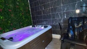 A modern bathroom with a large bathtub, a massage chair, and a green wall with plants.