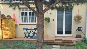 A house with a wooden deck, a tree, and a stone pathway leading to a door.