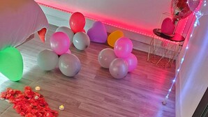 A wooden floor with a red flower petal path, balloons, and candles.
