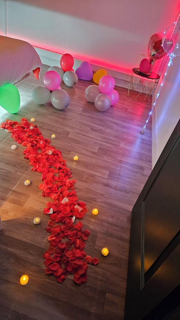 Un suelo de madera con un sendero de pétalos de flores rojas, globos y velas.