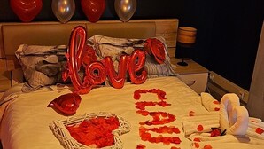 A bed with a heart-shaped balloon, rose petals, and the word "love" spelled out.