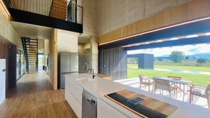 A modern kitchen with a large island, a dishwasher, and a view of a garden and outdoor seating area.
