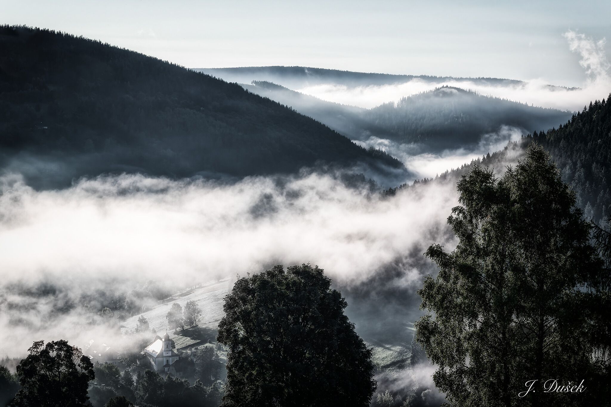 A mountainous landscape with a church and forested areas.