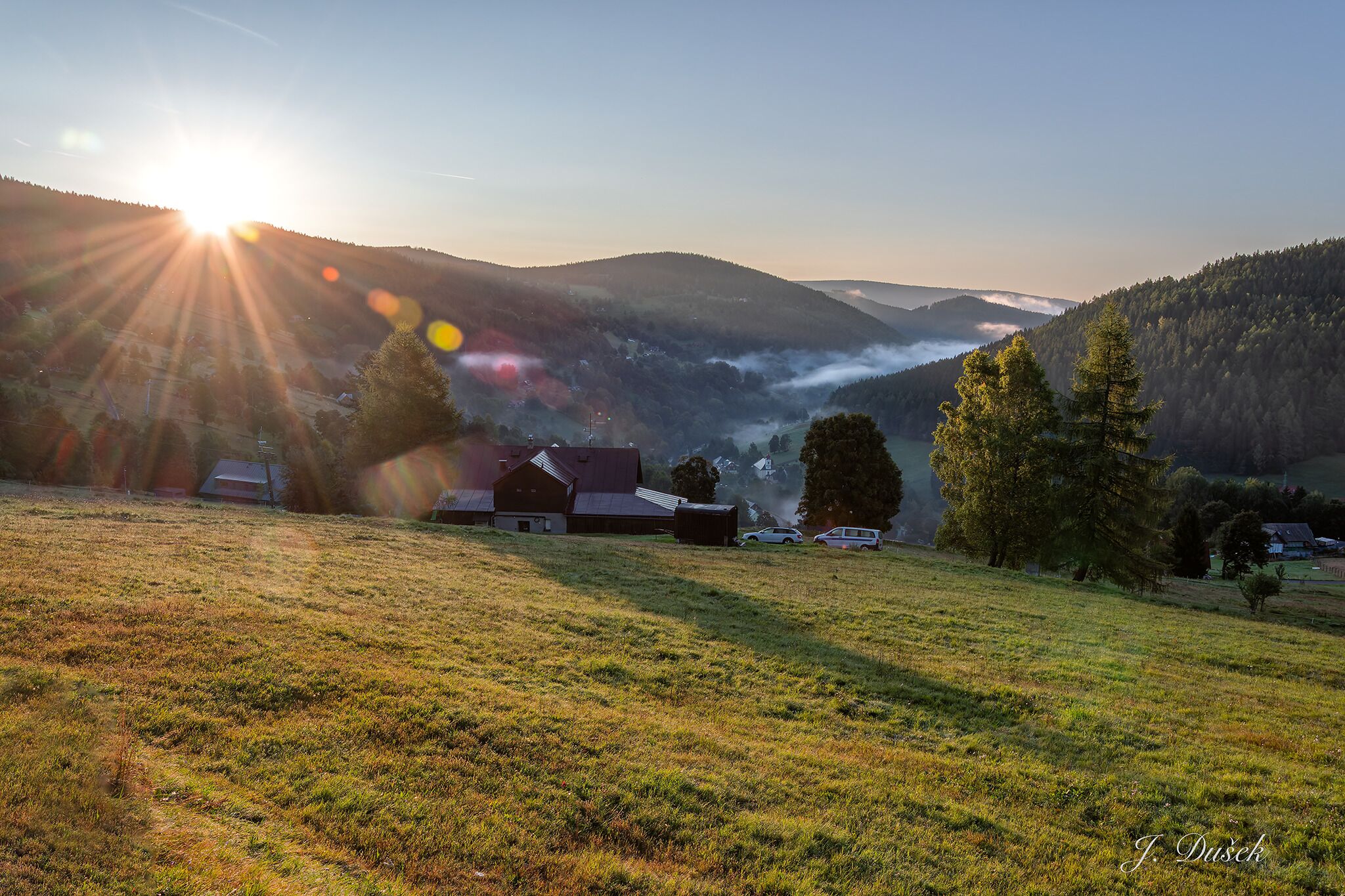 Ländliche Landschaft mit einem Bauernhof, Bäumen und sanften Hügeln.