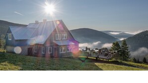 Una casa con techo inclinado, una terraza y vistas a una cadena montañosa cubierta de bosques.