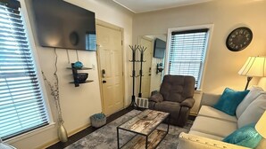 Ein Wohnzimmer mit einer Couch, einem Sessel, einem Couchtisch und einem an der Wand befestigten Fernseher.