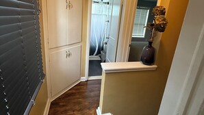 Ein Flur mit Holzboden, einer weißen Tür und einem kleinen Regal mit einer Vase.