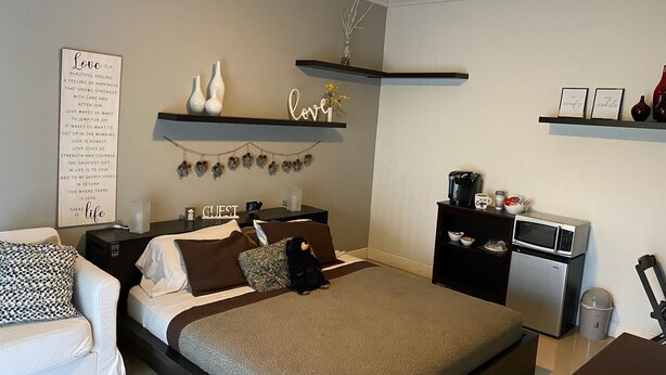 Une chambre moderne comprenant un lit, des tables de chevet, un coin café et une étagère murale agrémentée d’objets décoratifs.