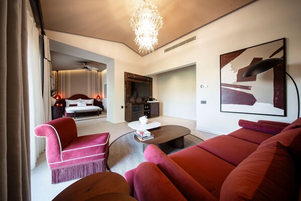 Una sala de estar moderna con un sofá, un sillón y una mesa de centro. Hay un televisor sobre un mueble bajo y una araña colgante sobre la zona de estar.