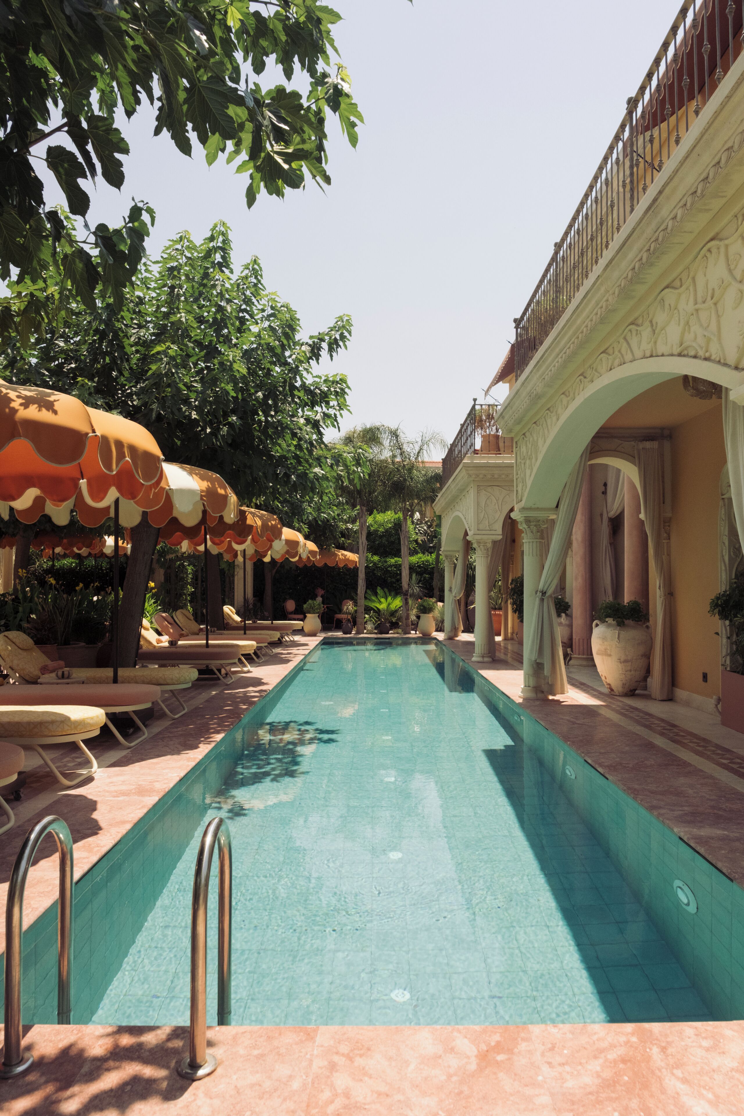 A swimming pool with sun loungers and umbrellas, surrounded by columns and arches.