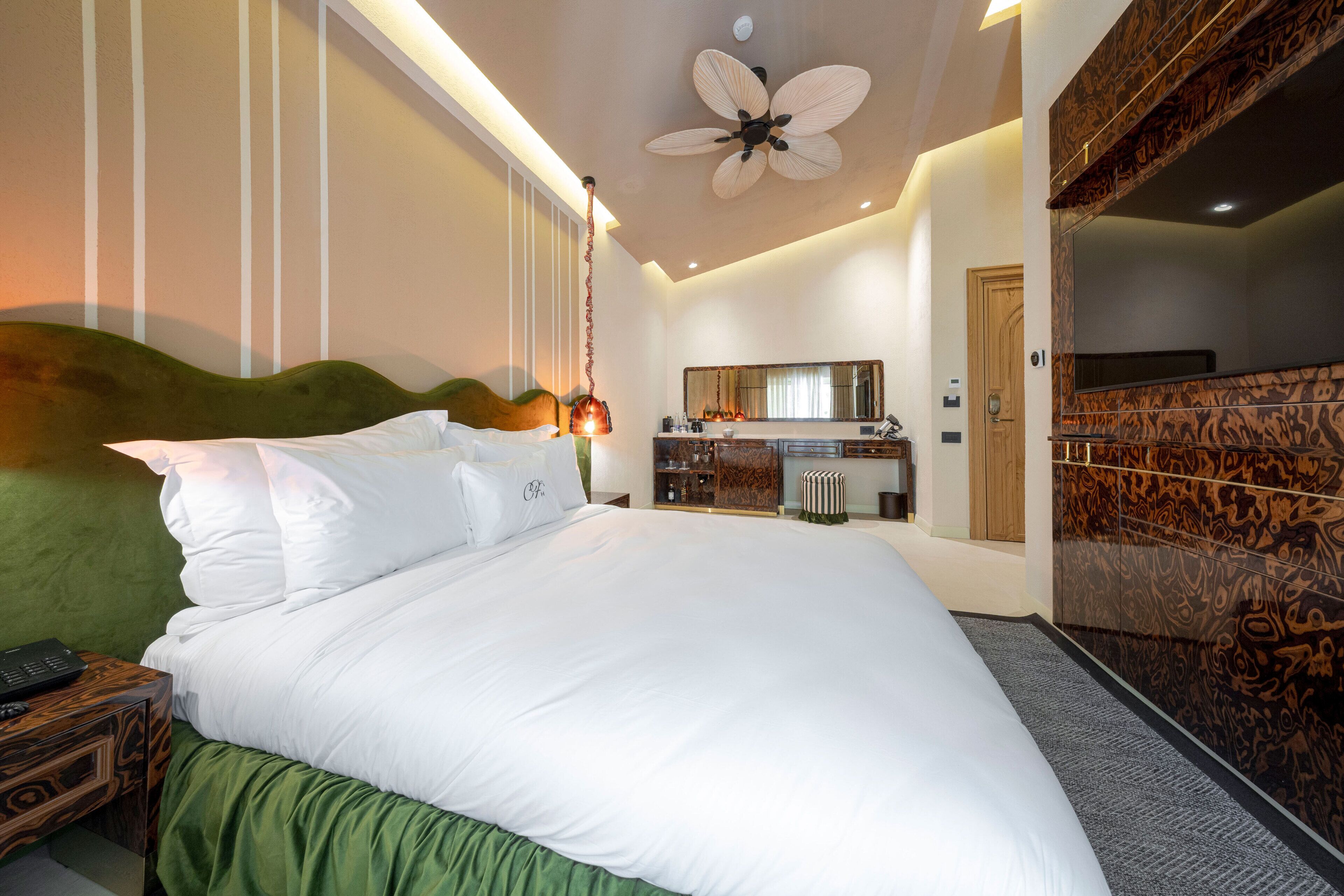 A modern hotel room with a large bed, a ceiling fan, a vanity with a mirror, and a bathroom with a shower and toilet.