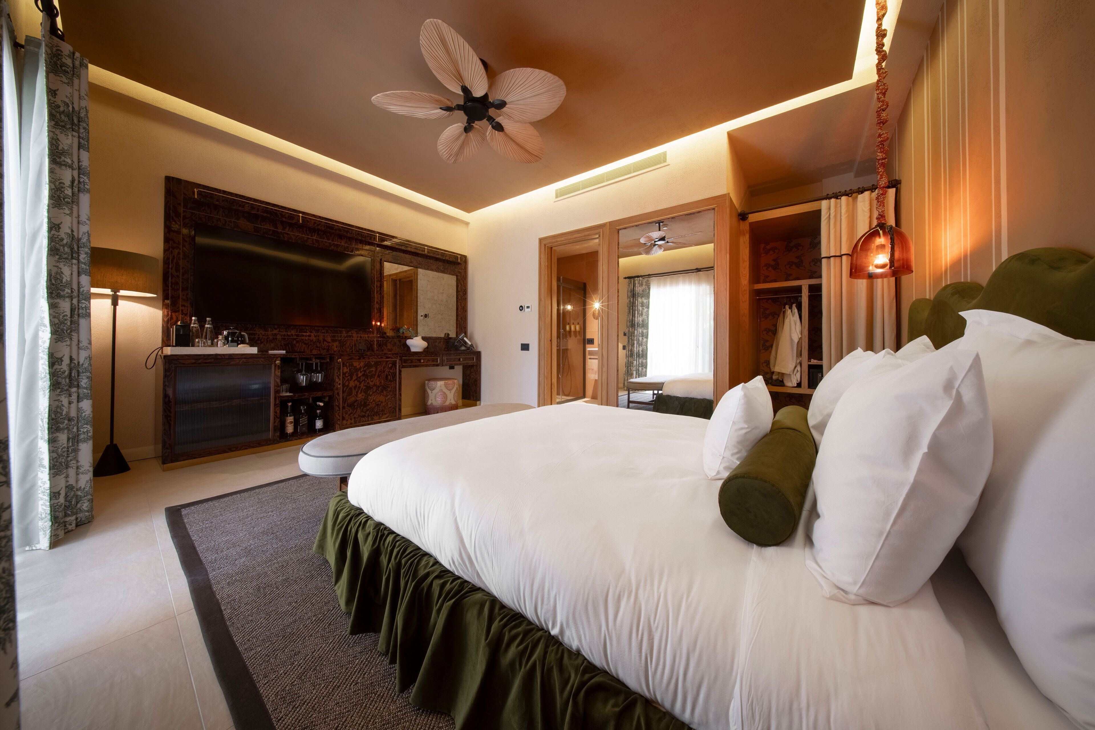 A spacious bedroom with a large bed, a ceiling fan, a flat-screen TV, a vanity with a mirror, and a walk-in closet.