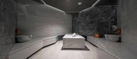 A modern bathroom with a central rectangular sink, marble walls, and a curved bench.