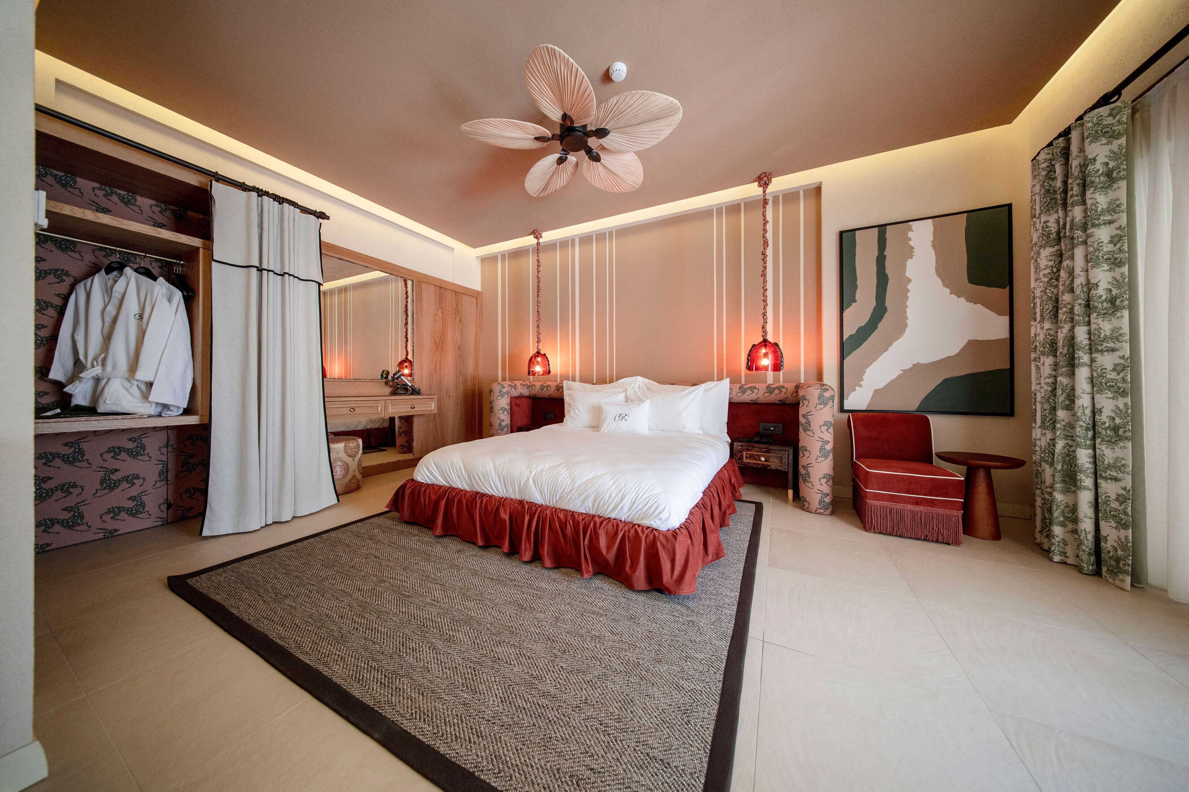 A spacious bedroom with a large bed, a ceiling fan, a wardrobe, and a bedside table with a lamp.