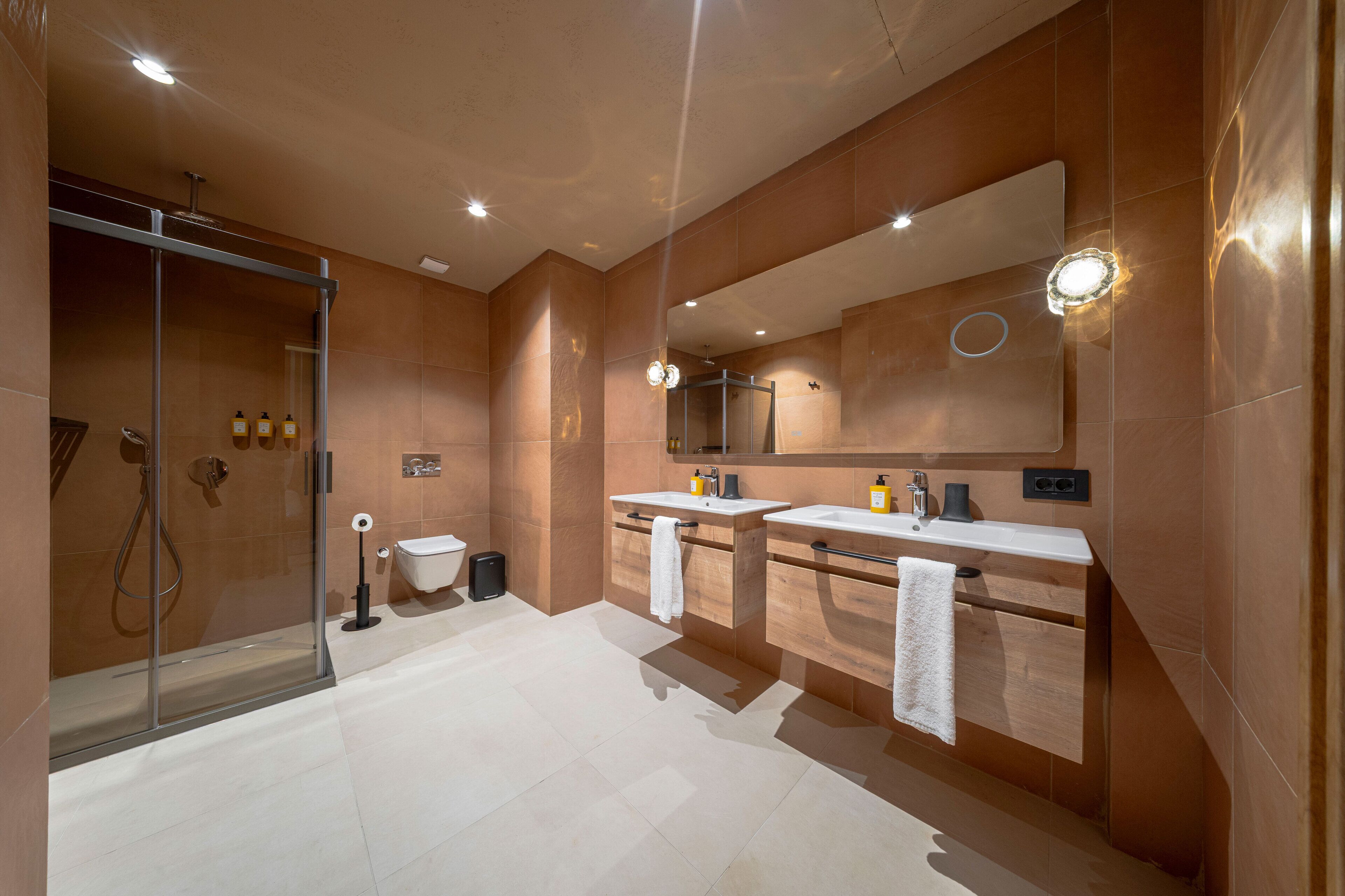Ein modernes Badezimmer mit einer gläsernen Dusche, zwei Waschbecken und einem großen Spiegel.