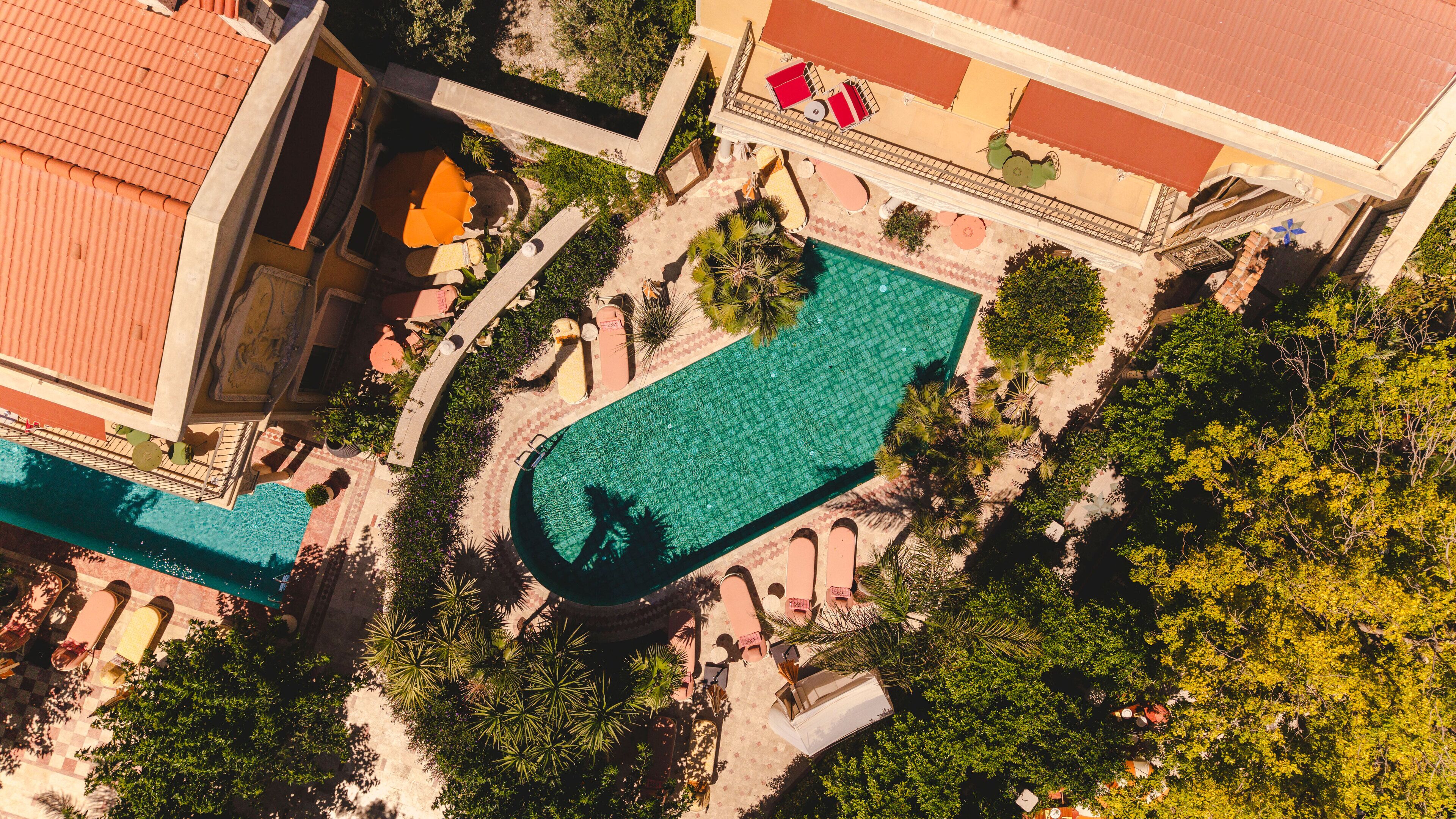 Vista aérea de un hotel con una amplia piscina, zonas de estar al aire libre y abundante vegetación.