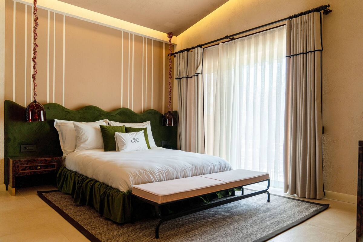 A neatly made bed with a green headboard, a bedside table, and a bench at the foot of the bed.