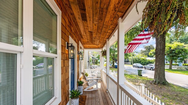 A wooden porch with a white railing, potted plants, and an American flag.
