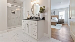A modern bathroom with a glass-enclosed shower, a vanity with a large mirror, and a wooden floor.