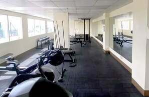 A gym with exercise equipment, large windows, and a mirrored wall. - Home Sweet Home at Makati (Makati)