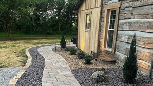 Un chemin de pierres mène à une maison en bois dotée d’une fenêtre et d’une porte.