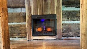 Une cheminée avec une façade en verre, intégrée dans l’intérieur d’un chalet en bois.